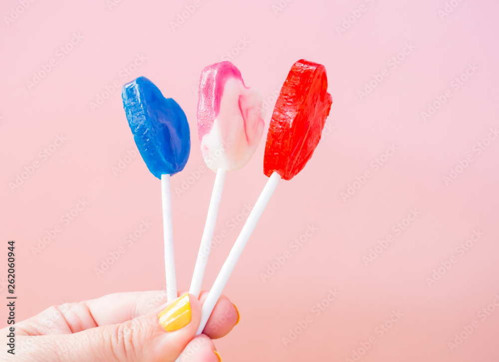 A woman with yellow painted nails with three different lollipop in her hand and pastel pink background A woman with yellow painted nails with three different lollipop in her hand and pastel pink background