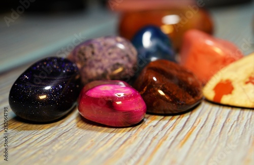 A variety of semi-precious stones of different minerals and structures on a wooden table. A collection of various polished gemstones © Elena