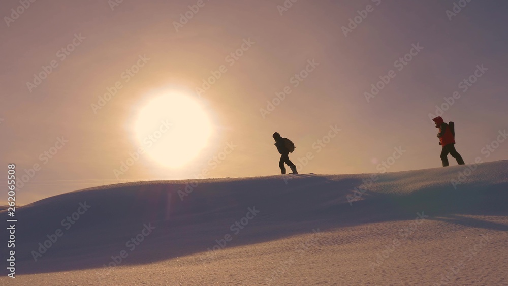 team of climbers follow each other along snow ridge in rays of yellow sunt. work in team of tourists, overcoming difficulties to move to victory and success. silhouettes of travelers go to victory