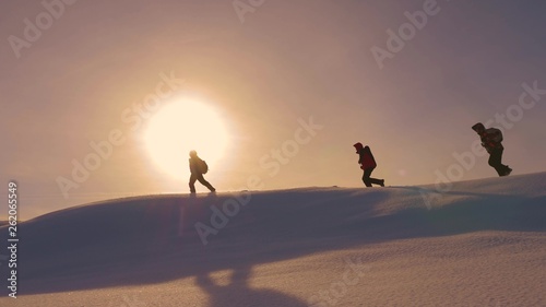 team of climbers follow each other along snow ridge in rays of yellow sunt. work in team of tourists, overcoming difficulties to move to victory and success. silhouettes of travelers go to victory