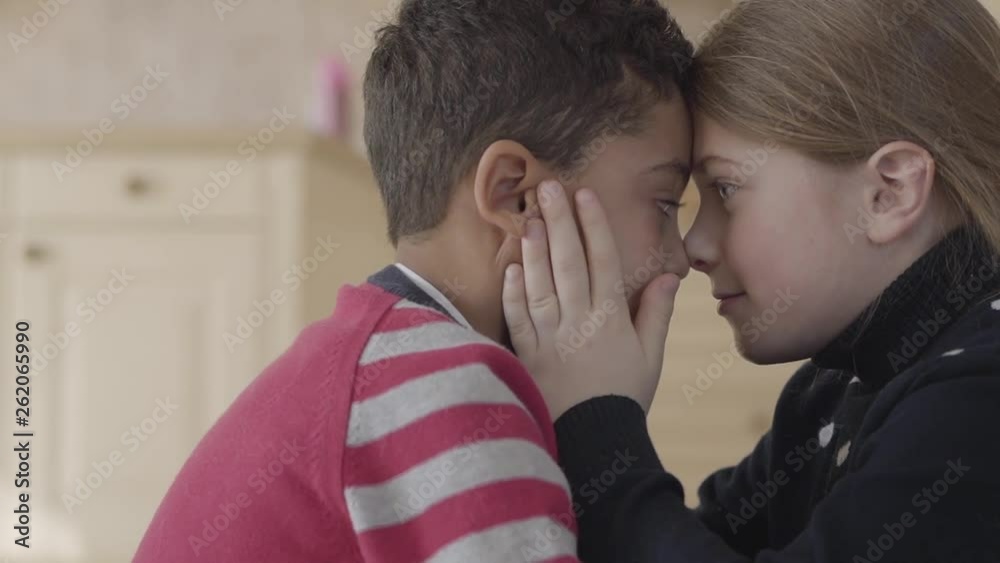 Portrait of handsome african american boy and pretty blond caucasian girl touching foreheads each other. Children recognize each other using tactile sensations. Girl hold boys face in hands Portrait of handsome african american boy and pretty blond caucasian girl touching foreheads each other. Children recognize each other using tactile sensations. Girl hold boys face in hands