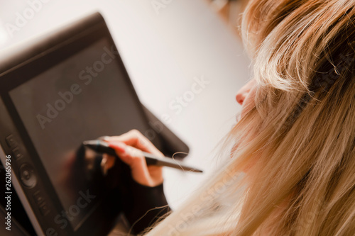 Young hipster graphic woman designer using digital graphic tablet, professional female retoucher sitting at workspace.