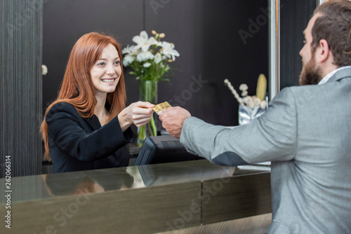 Businessman giving credit card to smiling female receptionist while standing at hotel reception desk