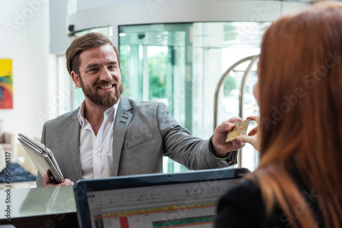 Smiling businessman giving credit card to female receptionist while standing at hotel reception desk