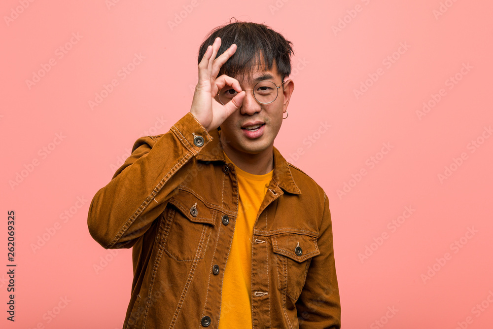 Young chinese man wearing a jacket confident doing ok gesture on eye Young chinese man wearing a jacket confident doing ok gesture on eye