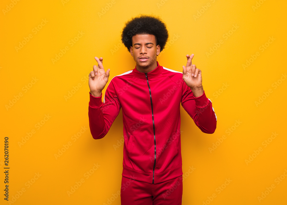 Young sport black man over an orange wall crossing fingers for having luck Young sport black man over an orange wall crossing fingers for having luck