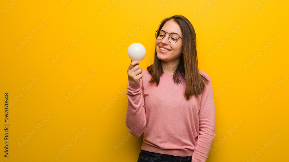 Young cute woman holding a light bulb cheerful with a big smile Young cute woman holding a light bulb cheerful with a big smile