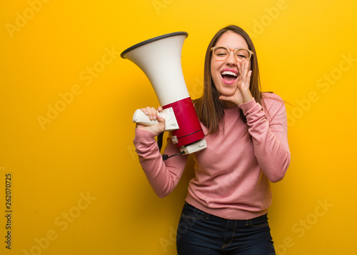 Cuadro en lienzo Young cute woman holding a megaphone shouting something happy to the front