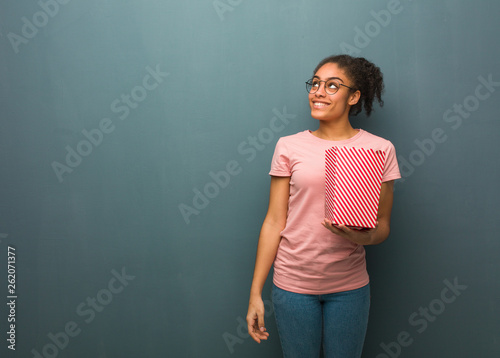 Young black woman dreaming of achieving goals and purposes. She is holding a popcorns bucket.