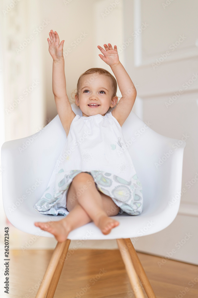 Portrait of smiling toddler girl sitting on a chair with raised hands Portrait of smiling toddler girl sitting on a chair with raised hands