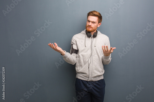 Young fitness redhead man confused and doubtful