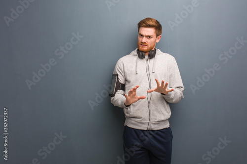 Young fitness redhead man rejecting something doing a gesture of disgust