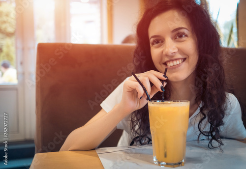 beautiful curly brunette girl drinks juice in cafe