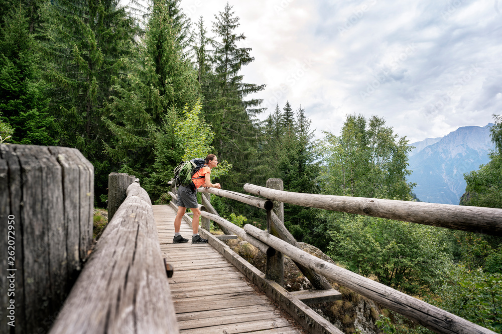 Switzerland, Valais, woman standing on a wooden bridge during a hiking trip on the Massaweg in the mountains Switzerland, Valais, woman standing on a wooden bridge during a hiking trip on the Massaweg in the mountains