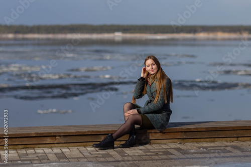 girl in a coat sitting in the background of the Volga river with floating ice floes.