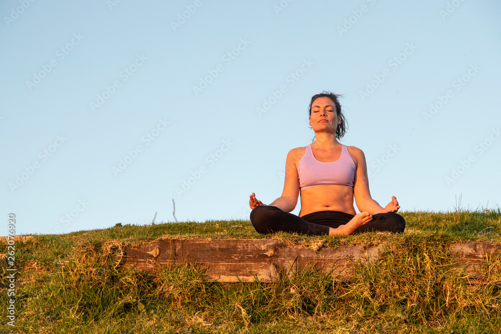 Woman meditating on a meadow in the evening Woman meditating on a meadow in the evening