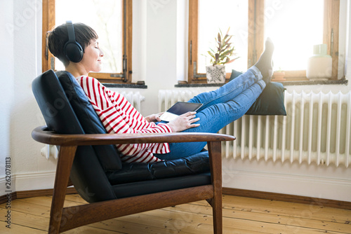 Short-haired woman with headphones relaxing in lounge chair in stylish apartment photo