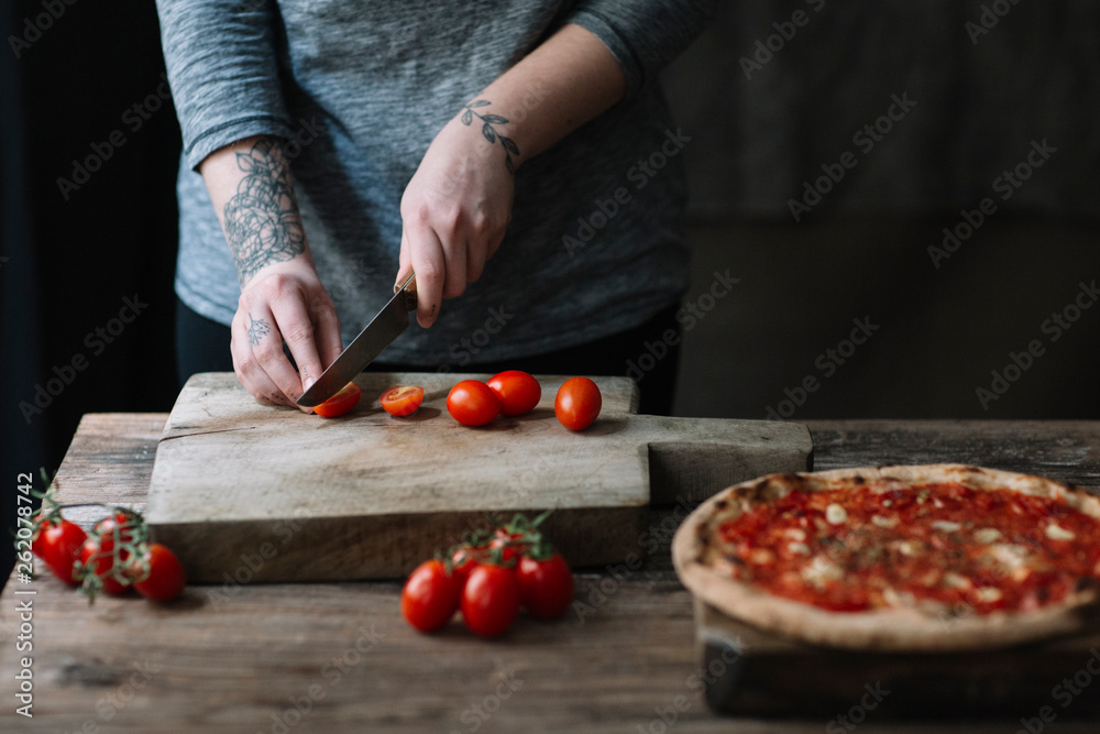 © Westend61 - Young woman preparing pizza, cutting tomatoes on chopping board
