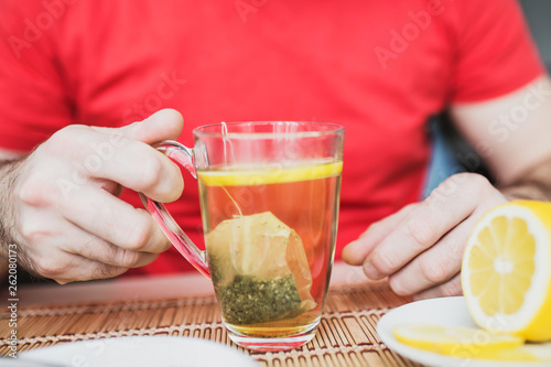 View of glass cup of tea with mint in male hand - lemon, honey and jam
