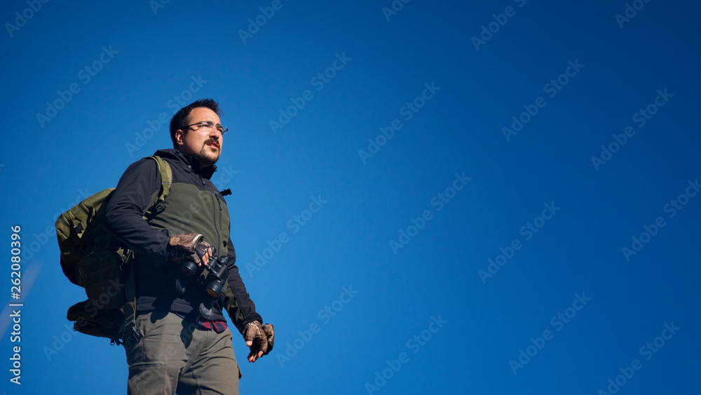Fototapeta premium hiker man on rocky mountain looking through binoculars