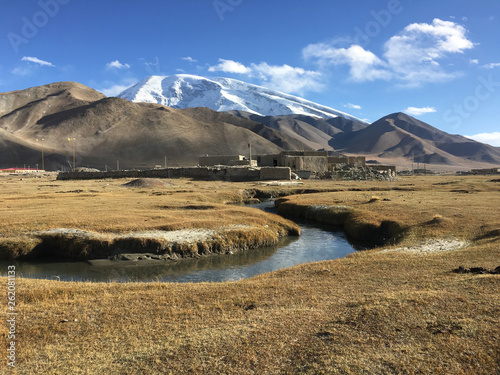 View on Muztagata mountain with buildings and river in the foreground (captured near Lake Karakul, Karakorum Highway, Xinjiang Province, China)  photo