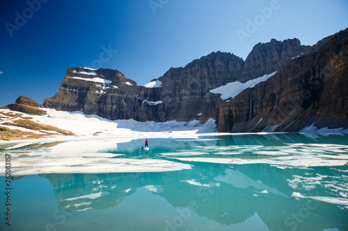 A woman stand up paddles (SUP) among floating chunks of ice on Upper Grinell Lake next to the remnants of the Grinell Glacier in Glacier National Park, Montana.         photo