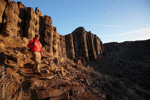 A man hikes into the Sunshine Wall area of the Frenchman-Coulee at sunrise in central Washington State. The impressive volcanic basalt columns are the remnants of lava flows that cooled once reaching the surface. The unique features of the columns make them a popular choice for rock climbers. photo