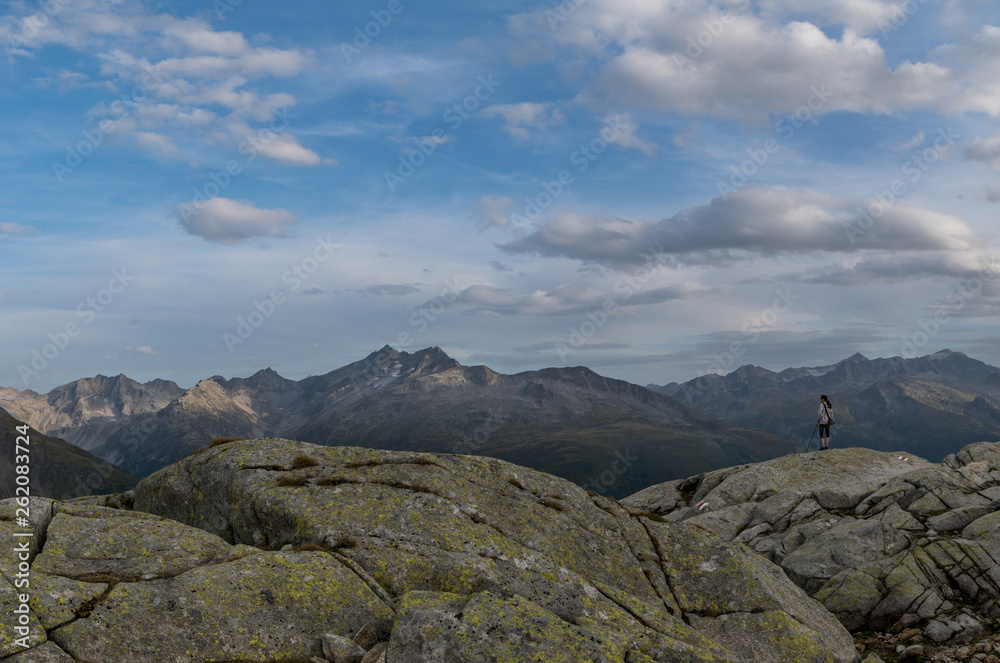 Fototapeta premium A girl on hiking trip in Swiss Alps enjoys the view down to the valley on the background of mountain ridge
