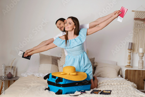 Ready for vacationl! Happy couple showing airplne with their hands, with suitcase, passports and tickets in their home having fun and happy future travel photo