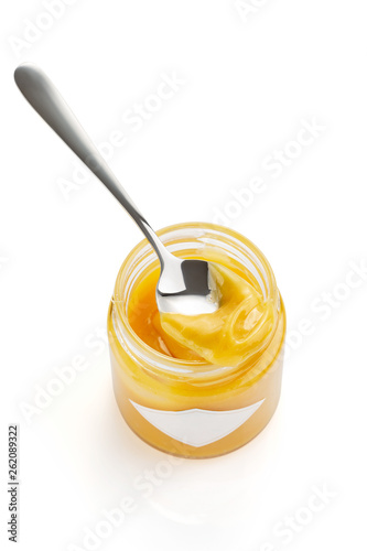 Spoon with homemade lemon curd on glass jar isolated on white background