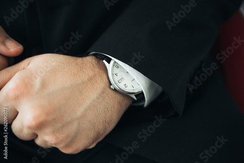 Close-up of fashion image of man's luxury watch on wrist. Businessman in black suit with watch on hand. Fastening a wristwatch. Body detail of a business man. Man's hand in a white shirt