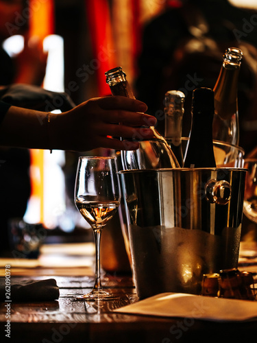 wine tasting: there is a glass of wine on a wooden table, and a silver bucket for cooling wines with open bottles of champagne, from which a bottle is taken out.