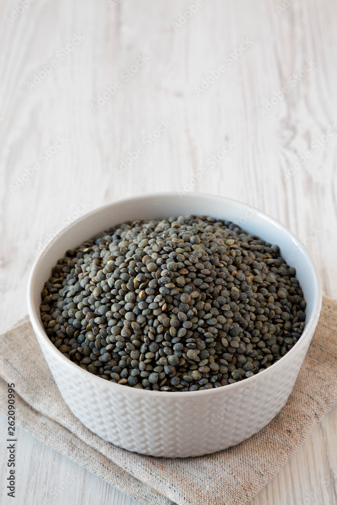 Green french lentils in a bowl over white wooden background, low angle view. Copy space. Green french lentils in a bowl over white wooden background, low angle view. Copy space.