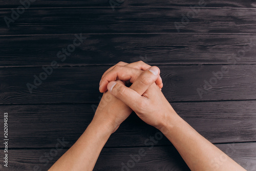 interlocked fingers, white male hands interlocked on black rustic wood table close up. top view. a man is waiting for negotiations