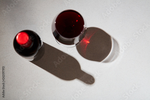 Top view of wine bottle and shiny glass of red wine on simple gray background