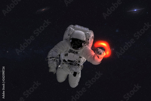 Space astronaut near black hole red glow. Space adventure in outer space. Science fiction. Elements of this image were furnished by NASA © ALEXANDR YURTCHENKO