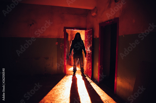 Creepy silhouette with knife in the dark red illuminated abandoned building. Horror about maniac concept