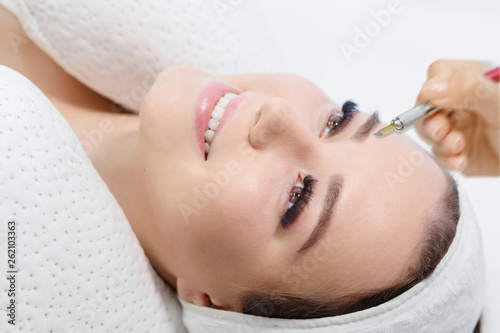 Beautiful young girl with long eyelashes tweezing her eyebrows in a beauty salon. Woman doing eyebrow permanent makeup correction. Microblading brow.