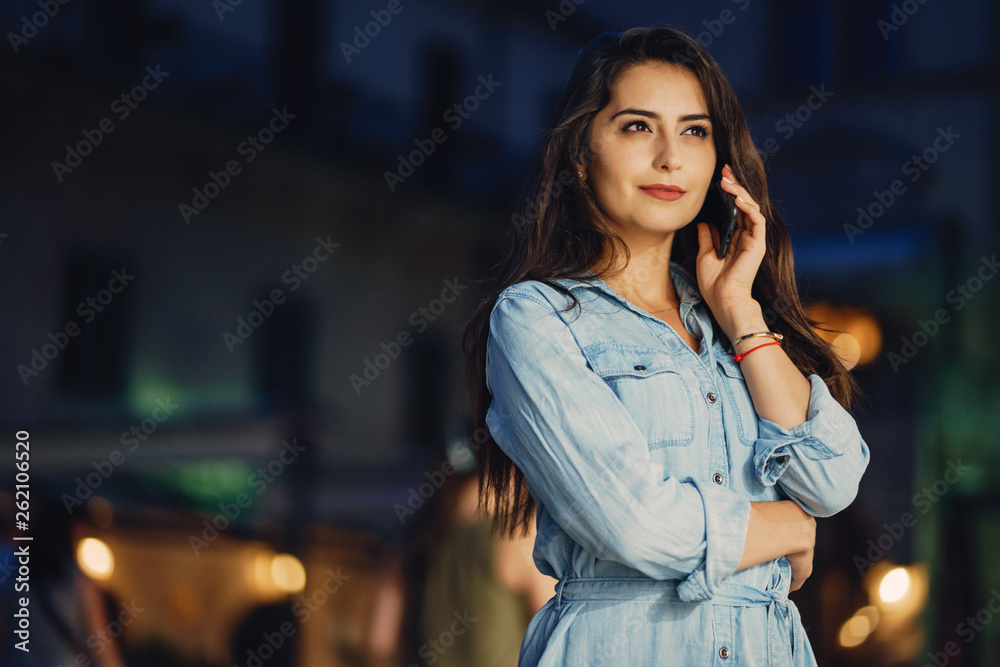 A beautiful young girl in a blue dress standing in a night city with phone A beautiful young girl in a blue dress standing in a night city with phone