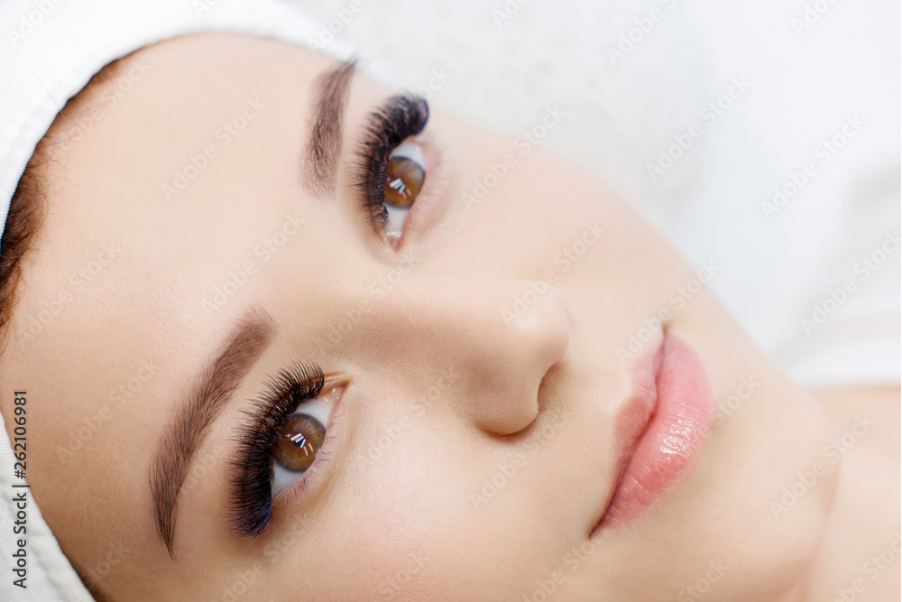 Eyelash extension procedure. Beautiful woman with long eyelashes and perfect glow clean skin. Facial treatment. Cosmetology, beauty, skin care, spa concept. Permanent makeup. Microblading brow.
