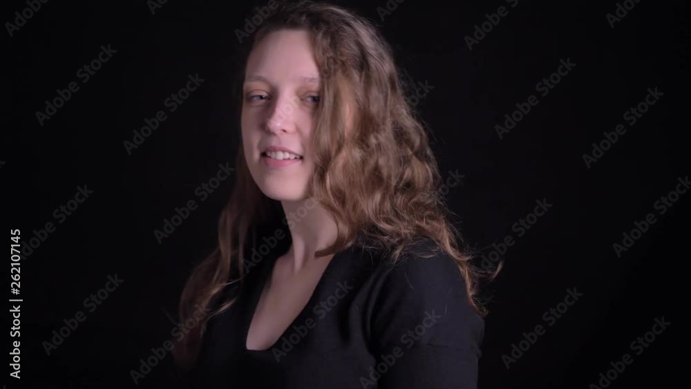 Portrait of modest young curly-haired girl flirting with camera and shaking her hair on black background. Portrait of modest young curly-haired girl flirting with camera and shaking her hair on black background.