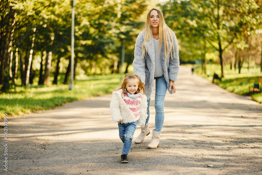 young blonde mother running behind her super energetic toddler daughter in a sunny park young blonde mother running behind her super energetic toddler daughter in a sunny park