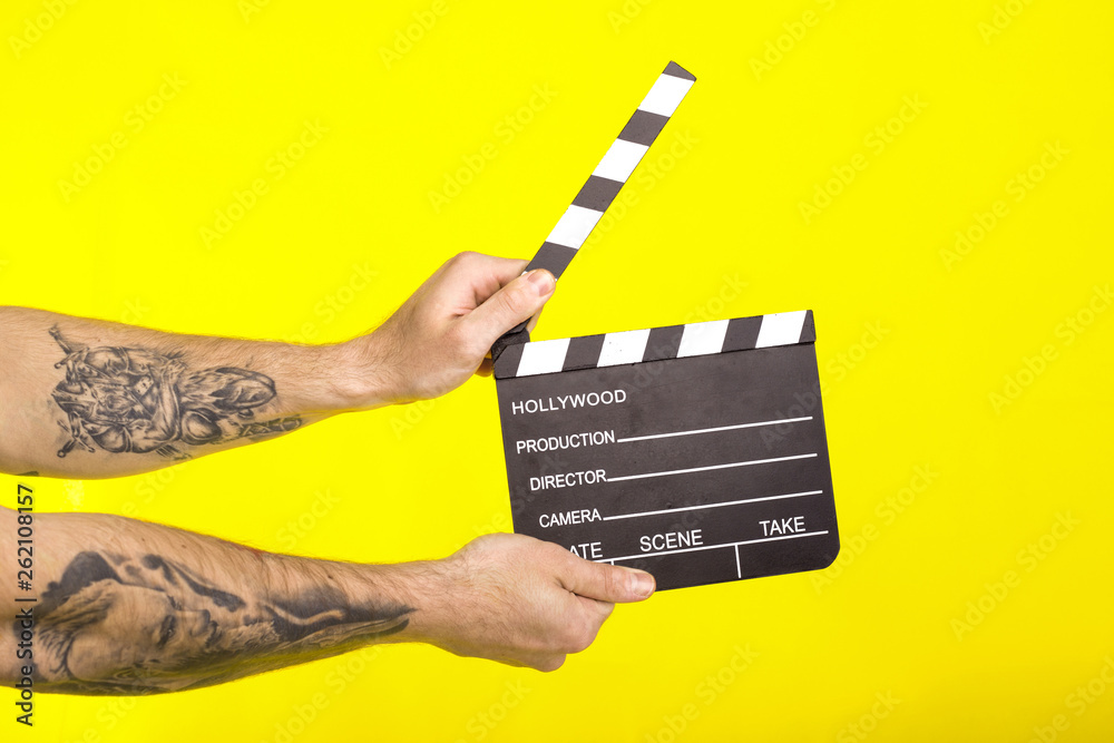 director's clapper. hands with a boardсlapper on a yellow background.