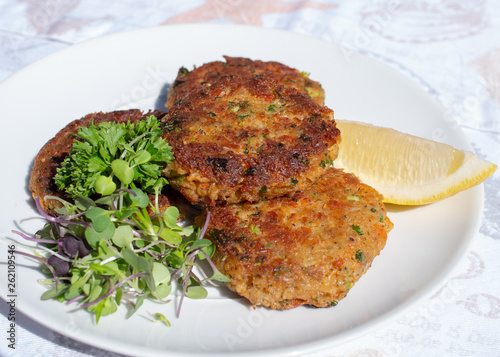 Fresh crab cakes served on a white plate with lemon and salad.