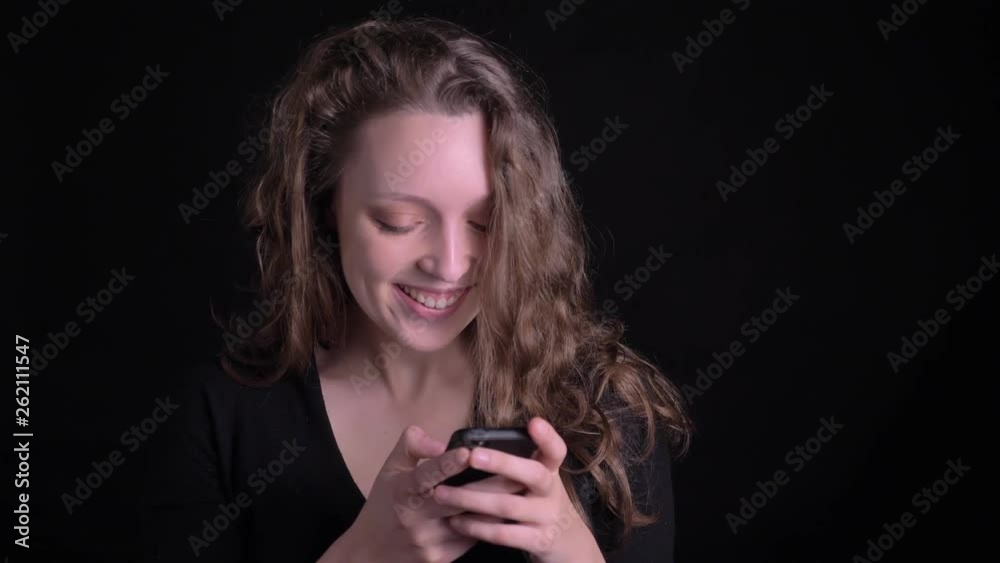 Portrait of young curly-haired girl watching gladly into smartphone on black background. Portrait of young curly-haired girl watching gladly into smartphone on black background.