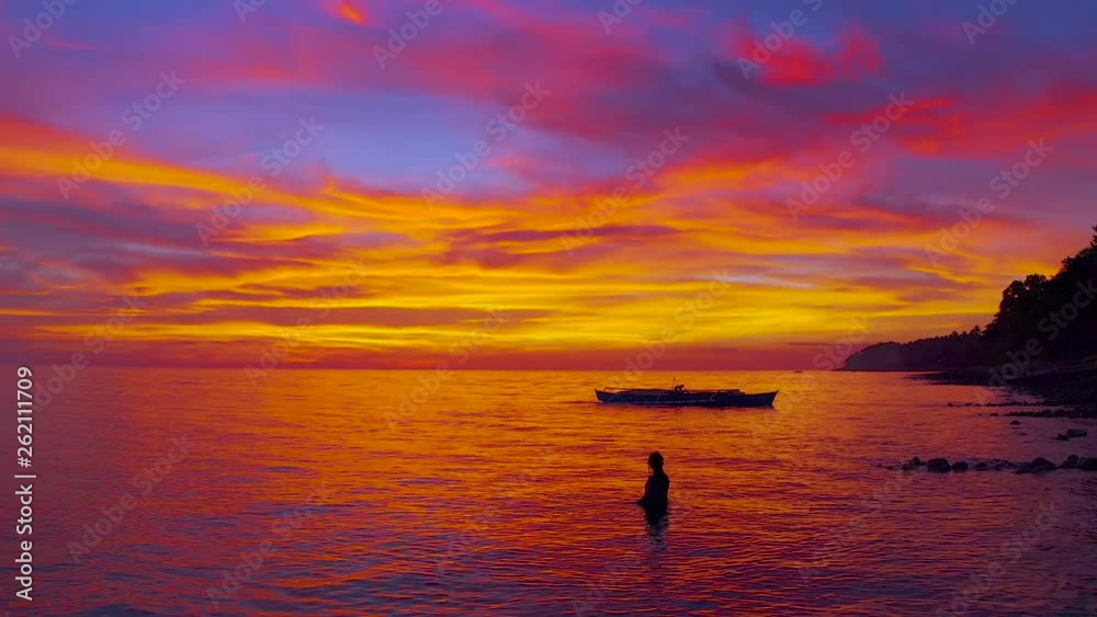 Free diving girl snorkeling in the sea reflecting crazy orange-yellow-pink sky looking like melted red hot metal on the background of the sea horizon and fisherman's boat silhouette, Philippines Free diving girl snorkeling in the sea reflecting crazy orange-yellow-pink sky looking like melted red hot metal on the background of the sea horizon and fisherman's boat silhouette, Philippines
