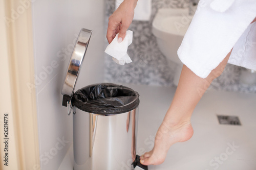 Close up of foot pressing a pedal to open cap of garbage bin. Young woman doing cleaning in the bathroom. Personal hygiene.