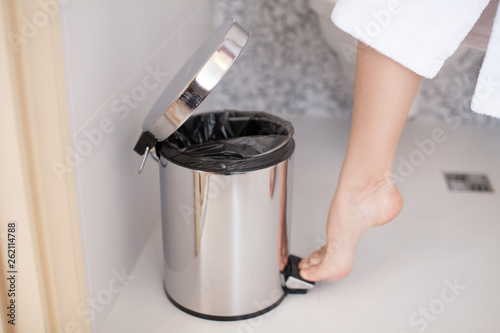 Close up of foot pressing a pedal to open cap of garbage bin. Young woman doing cleaning in the bathroom. Personal hygiene. photo