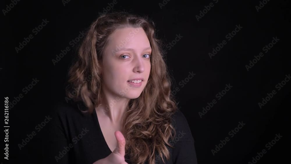 Young curly-haired girl gesturing finger-up showing like and respect with mysterious smile into camera on black background. Young curly-haired girl gesturing finger-up showing like and respect with mysterious smile into camera on black background.