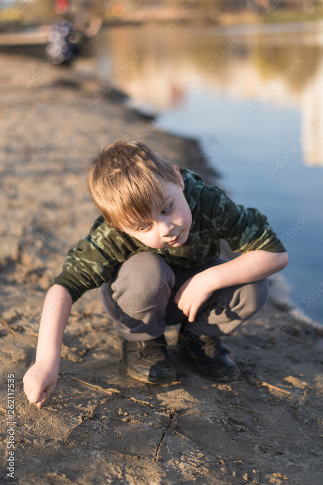 A little boy plays on the shore of a pond while digging in the sand. A little boy plays on the shore of a pond while digging in the sand.